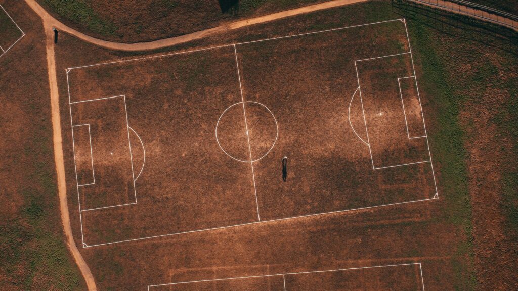 Aerial view of an empty rustic soccer field with a solitary person, showcasing detailed grass lines.
